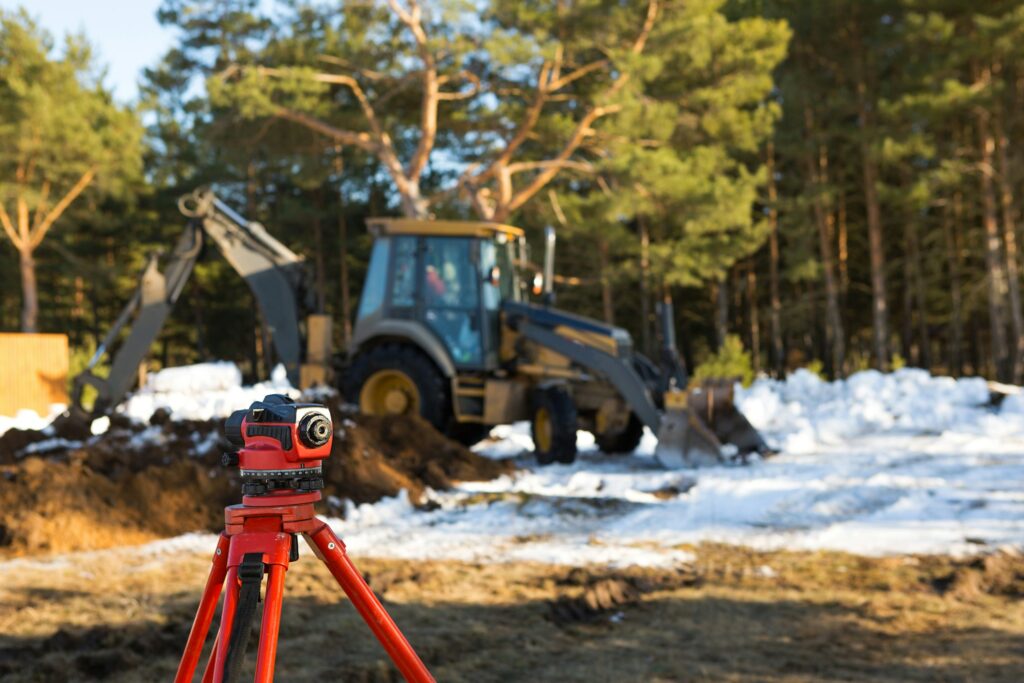 A geodesic level stands in front of a bulldozer for excavating a pit at a construction site.